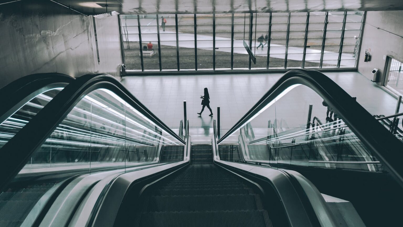 People using the sleek modern escalator in an indoor building with glass panels.