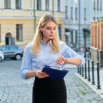 Młoda biznesowa kobieta w mieście patrząc na jej zegarek na rękę. Pewna siebie, poważna kobieta z papierami w dłoniach idąca ulicą