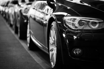 Close-up black and white image of a luxury car line-up focusing on vehicle headlights.