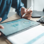 Profesjonalista biznesowy analizujący dane finansowe na cyfrowym panelu tabletu, z kalkulatorem i laptopem, symbolizujący oprogramowanie księgowe, integrację z systemem ERP oraz monitorowanie wyników