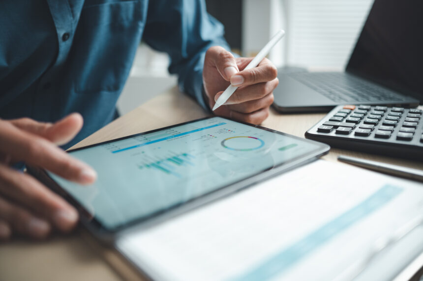 Profesjonalista biznesowy analizujący dane finansowe na cyfrowym panelu tabletu, z kalkulatorem i laptopem, symbolizujący oprogramowanie księgowe, integrację z systemem ERP oraz monitorowanie wyników