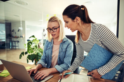 Dwóch młodych współpracowników biznesowych pracujących razem przy biurku w biurze, omawiających dokumenty i korzystających z laptopa